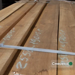 Close-up of stacked edged spruce boards with handwritten chalk dimensions and a white packing strap.