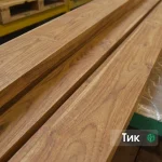 Close-up of stacked 1st grade edged teak boards showing their rich golden-brown grain.