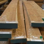 Stacked edged teak lumber boards of extra grade with marked dimensions on the ends.
