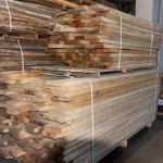 Multiple large stacks of dried edged ash lumber stored in a spacious woodworking warehouse.