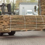 A forklift transporting a large bundle of ash boards in an industrial yard.