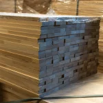 End grain and joint pattern of stacked finger-jointed beech boards in a warehouse.