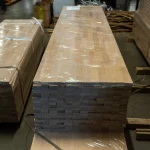 A long stack of beech furniture panels wrapped in protective plastic film.