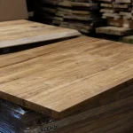 Solid oak furniture board placed on top of a stack of lumber in a woodworking shop.