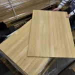 A worker holding a finished solid-lamella oak furniture panel over a stack in the warehouse.