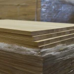 A stack of oak furniture panels wrapped in protective plastic film, showing the clean side edges.