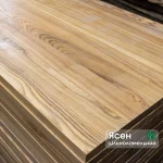 Top view of stacked solid-laminated ash furniture panels showing rich natural wood grain.