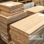 Stack of solid-lamella ash edge-glued panels in a warehouse with a product label.