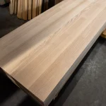 Long solid ash edge-glued panel lying on a pallet in a woodworking warehouse.