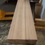 Top-down view of a long, wide solid-lamella ash panel showcasing its uniform color and grain.