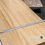 Close-up of a solid-lamella ash furniture board with a measuring tape showing its width and beautiful natural wood grain.