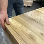 Close-up of a hand touching the smooth corner of a 40mm thick solid ash panel.