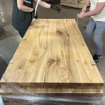 Workers packaging a stack of solid ash furniture panels on a pallet in the warehouse.