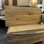 Two workers holding a solid ash furniture board above a stack in the workshop.