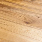 Close-up of a natural dark knot and swirling grain on a rustic ash furniture board.