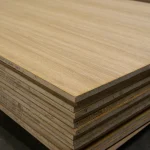 A stack of oak veneered blockboard sheets in a warehouse, showing the side profiles and top surface.