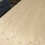 Angled view of the wide surface of a solid-lameled pine board showing knots and staves.