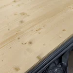 Detailed texture of the solid-lameled pine board surface with natural wood knots.