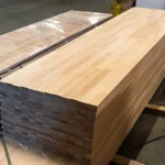 Long stack of finished finger-jointed beech furniture panels in a woodworking warehouse.