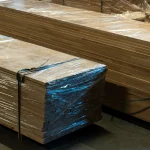 Stacks of beech furniture panels wrapped in protective plastic film for shipping.