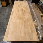 Long finger-jointed oak furniture board laid out on a workbench in the workshop.