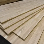 Several finger-jointed oak furniture boards stacked diagonally in a warehouse.