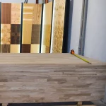A stack of 20mm finger-jointed oak panels in a workshop with a measuring tape on the top panel.