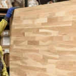 Worker holding a vertical finger-jointed oak panel, showing the joint pattern.