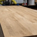 Perspective view of a large 3x0.8m finger-jointed oak panel on a workshop table.