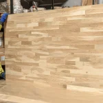 Worker holding a large finger-jointed oak furniture panel in a warehouse.