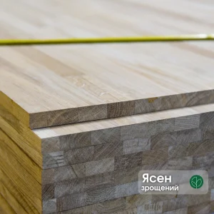 Close-up of stacked finger-jointed ash furniture boards showing the 20mm edge profile and wood grain.