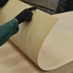 Процес згинання листа фанери гнучкої 2 мм із сейби рукою в рукавичці.