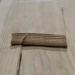 Edge of a sliced oak veneer bundle showing the 1.5 mm sheet thickness
