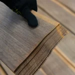 Showing the 0.6 mm thickness of a sliced American walnut veneer sheet held in a gloved hand.