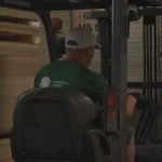WoodWay Expert warehouse worker on a forklift among wood materials.