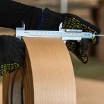 Штангенциркуль у руках вимірює ширину стрічки кромки зі шпону дуба